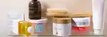 products lined up on a shower shelf: dr dennis gross alpha beta exfoliating body treatment, costa brazil firming oil, sans ceuticals activator 7 oil, goop g tox body scrub, goop dry body brush, drunk elephant koffie scrub, sol de janeiro bom dia bright cream and kylie beauty coconut body scrub