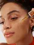 close up of side of a girl's face showing her applying face oil from a dropper onto her cheek
