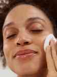 close up of a girl smiling and closing her eyes while wiping her cheek with cotton round