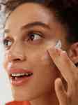 close up of a girl looking to the side smiling and applying face cream on her cheek