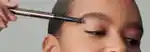model applying hourglass arch brow pencil to her eyebrow and looking to the side