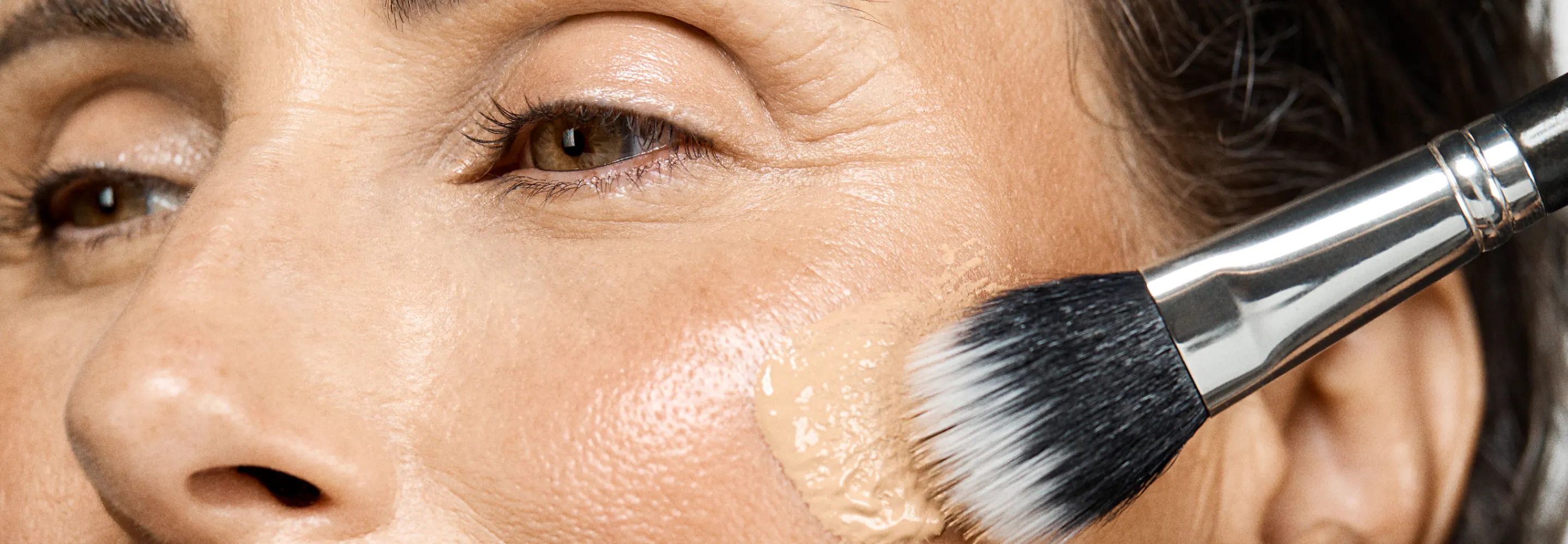 a model applying foundation to their cheek with a stippling brush