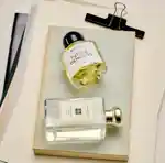 A split image of fragrance bottles on paper, and two hands passing a bottle