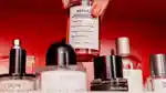 A hand with painted fingernails reaches down to lift a fragrance bottle from a shelf full of many bottles.