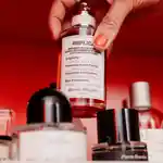 A hand with painted fingernails reaches down to lift a fragrance bottle from a shelf full of many bottles.