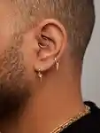 Close-up of a 'Curated Ear' – an ear with many piercings – on a male model.