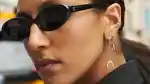 Close-up of a model wearing sunglasses, showing off her many Maria Tash ear piercings, on a New York street.