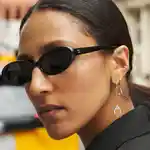 Close-up of a model wearing sunglasses, showing off her many Maria Tash ear piercings, on a New York street.