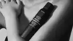 Black and white image of female model with bottle of sunscreen mousse in the crook of her arm.