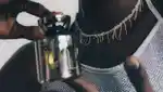 A male model wearing silver necklace and top holds silver bottle of Vyrao's perfume, The Sixth.
