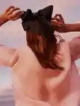 A female model, seen from behind, dressed in pink tightens the bow in her hair.