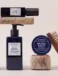 Murdock Barbers Of London Beard Oil positioned on top of Beard Shampoo with Beard Balm on the right side next to a brush